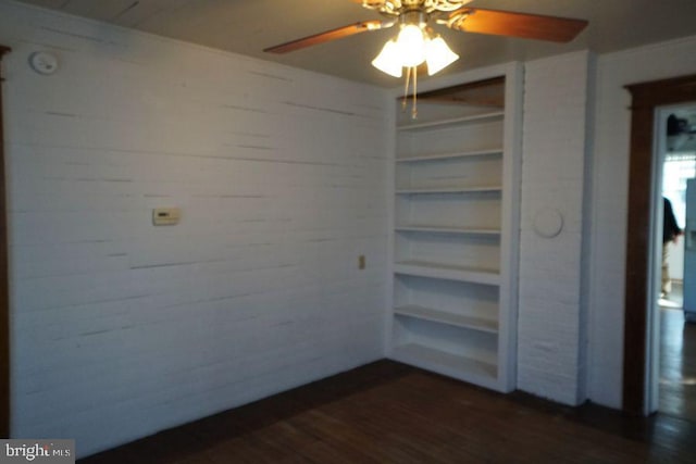 unfurnished room with ceiling fan, built in shelves, wood walls, and dark wood-style flooring