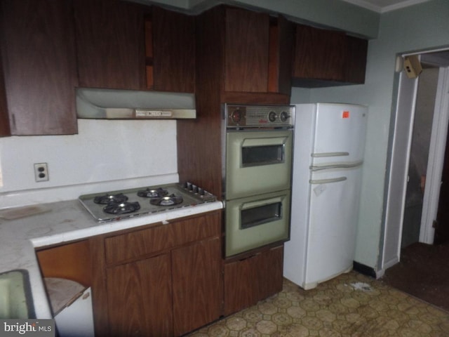 kitchen with multiple ovens, freestanding refrigerator, light countertops, extractor fan, and stainless steel gas cooktop