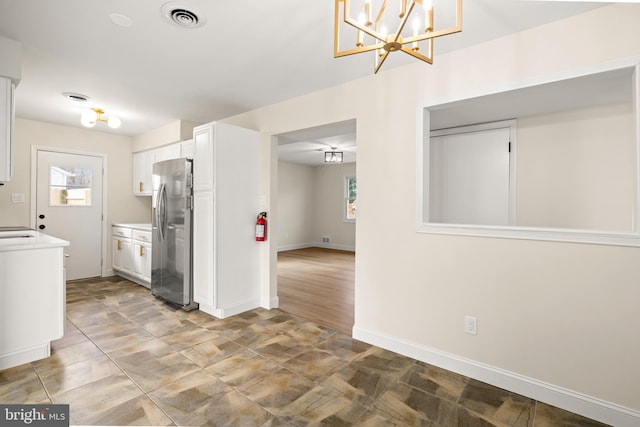 kitchen with visible vents, baseboards, light countertops, stainless steel fridge, and white cabinetry