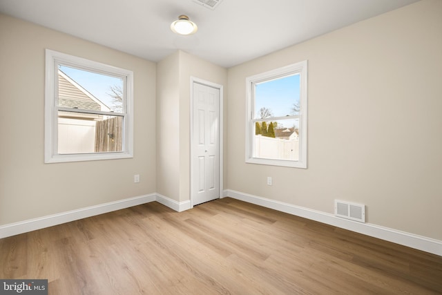 unfurnished bedroom featuring multiple windows, baseboards, visible vents, and light wood finished floors