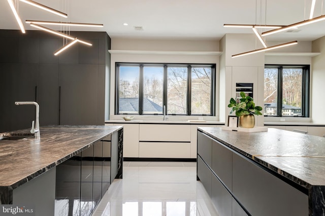 kitchen featuring a sink, an island with sink, dark stone countertops, white cabinetry, and modern cabinets