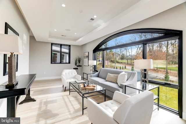 living area featuring baseboards, visible vents, recessed lighting, a raised ceiling, and light wood-type flooring