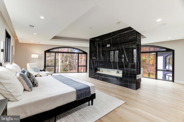 bedroom featuring visible vents, multiple windows, a tile fireplace, and wood finished floors