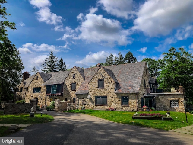 view of front of home with stone siding, a chimney, and a front lawn