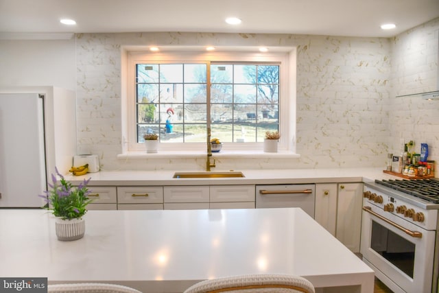 kitchen featuring high end white range, a sink, white cabinets, light countertops, and decorative backsplash