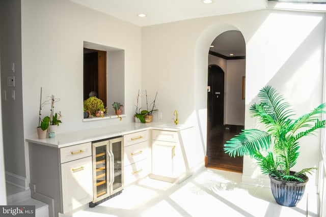 bar with baseboards, beverage cooler, recessed lighting, light wood-style floors, and arched walkways