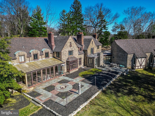 back of property with stone siding, a fire pit, a chimney, and a patio