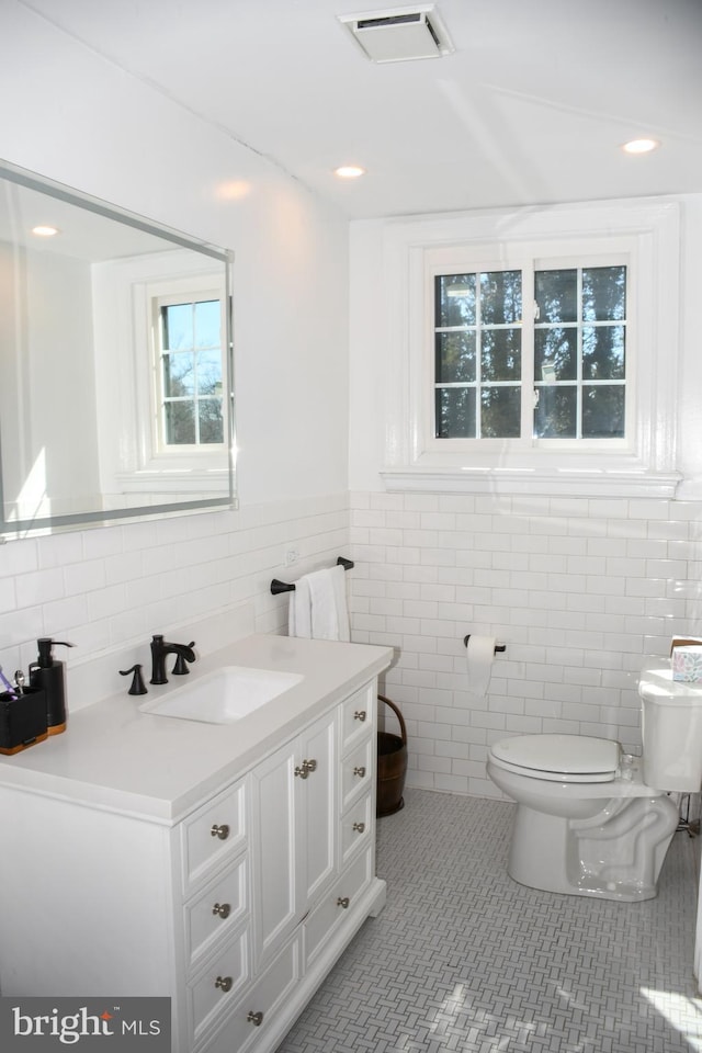 half bath featuring visible vents, tile walls, toilet, tile patterned floors, and vanity