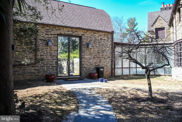 doorway to property featuring stone siding and roof with shingles