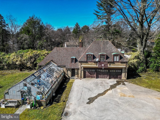 view of front of house featuring a greenhouse, an outbuilding, concrete driveway, and a chimney