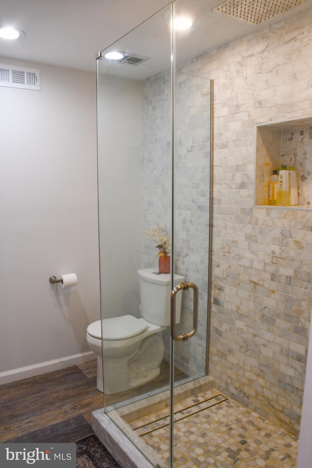 bathroom with visible vents, toilet, wood finished floors, a shower stall, and baseboards