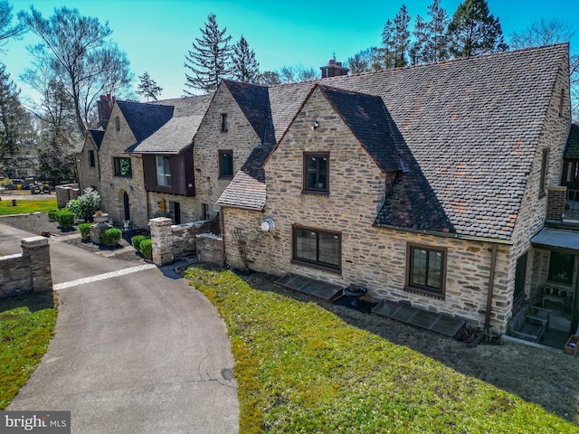 view of front of home with stone siding, a chimney, a high end roof, and a front yard