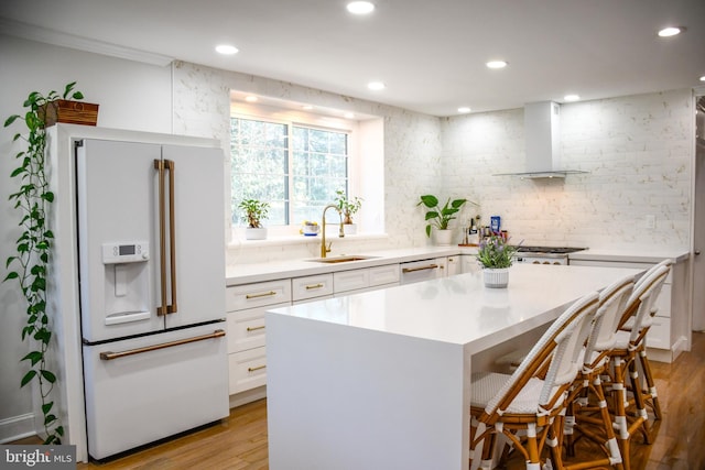 kitchen with white appliances, a sink, a kitchen breakfast bar, white cabinetry, and wall chimney range hood