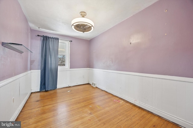 spare room with visible vents, wood-type flooring, and wainscoting