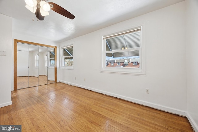 unfurnished bedroom featuring baseboards, multiple windows, a closet, and hardwood / wood-style flooring