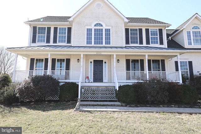 colonial inspired home featuring a porch, metal roof, a front yard, and a standing seam roof