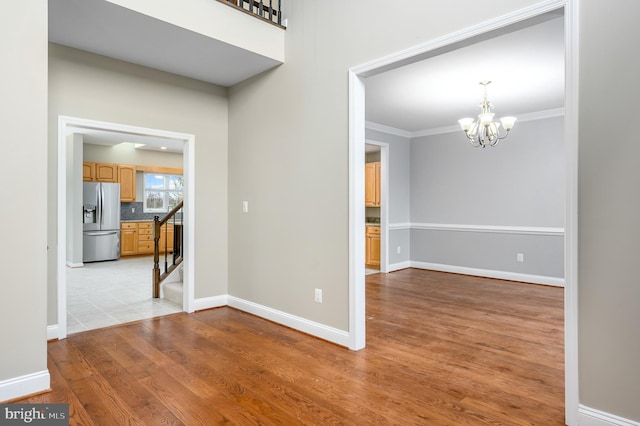 interior space with baseboards, an inviting chandelier, ornamental molding, and light wood finished floors