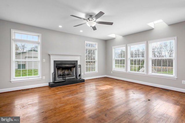 unfurnished living room featuring visible vents, baseboards, a fireplace with raised hearth, hardwood / wood-style flooring, and a ceiling fan
