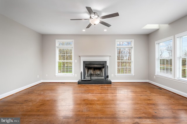unfurnished living room with baseboards, a fireplace with raised hearth, a ceiling fan, and wood finished floors
