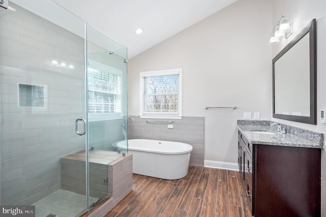 full bath with vanity, a shower stall, wood finished floors, lofted ceiling, and a soaking tub