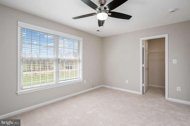 unfurnished bedroom featuring light carpet, a walk in closet, a ceiling fan, baseboards, and a closet