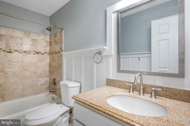 full bathroom featuring wainscoting, a decorative wall, vanity, toilet, and shower / bathing tub combination