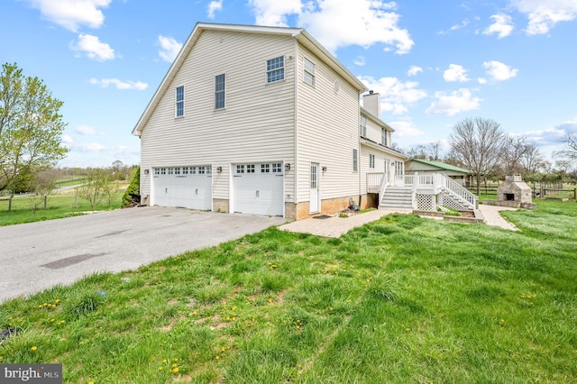 view of property exterior with driveway, a chimney, a wooden deck, a garage, and a yard