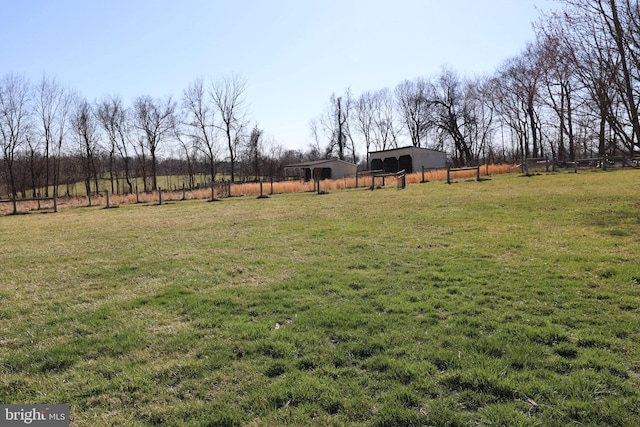 view of yard featuring fence, a pole building, an outbuilding, and a rural view