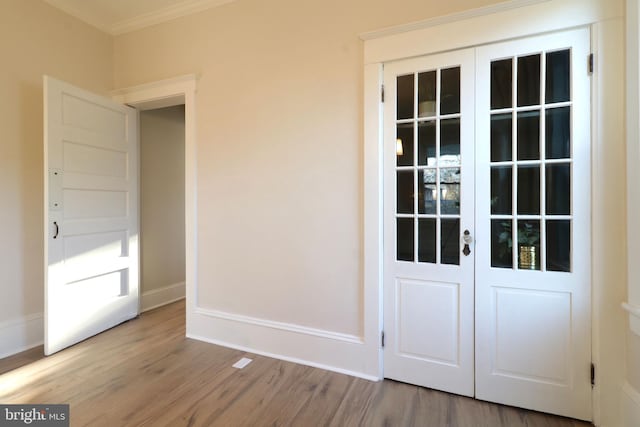 doorway featuring crown molding, wood finished floors, and baseboards