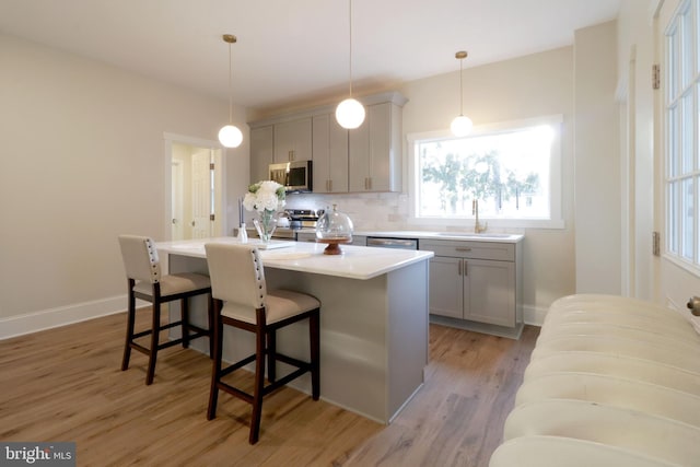 kitchen with gray cabinets, a sink, a kitchen breakfast bar, tasteful backsplash, and appliances with stainless steel finishes