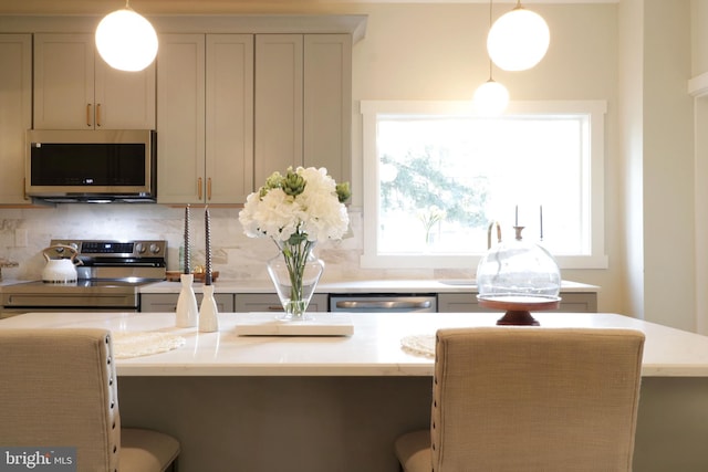 kitchen with hanging light fixtures, a kitchen breakfast bar, backsplash, and stainless steel appliances