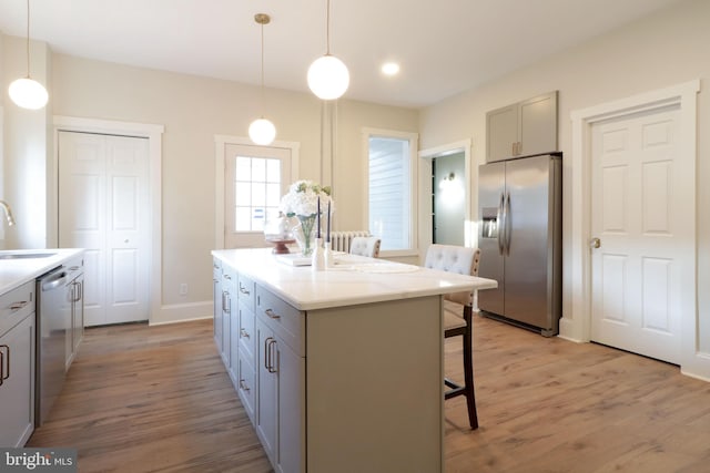 kitchen with a breakfast bar area, gray cabinets, a sink, stainless steel appliances, and light wood-style floors