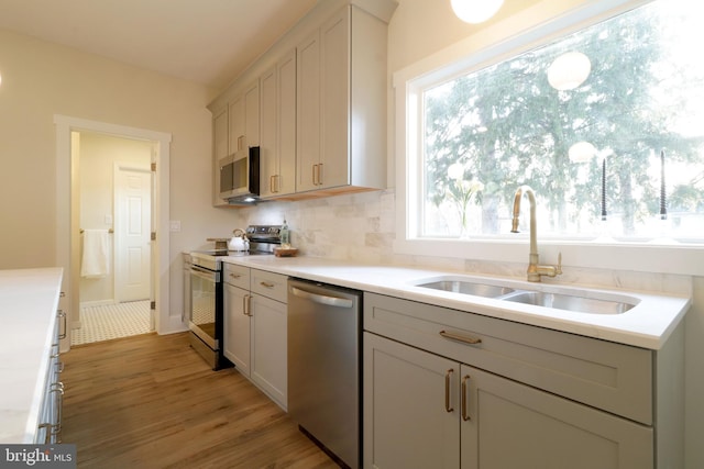 kitchen with light wood finished floors, light countertops, decorative backsplash, appliances with stainless steel finishes, and a sink