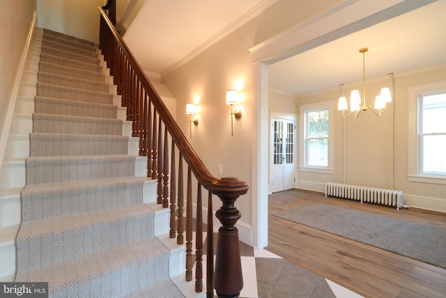 stairway with a notable chandelier, wood finished floors, radiator heating unit, crown molding, and baseboards