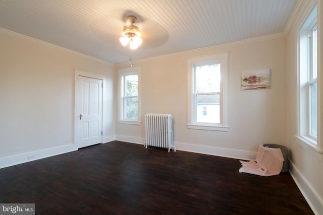 spare room featuring dark wood-type flooring, a healthy amount of sunlight, radiator heating unit, and crown molding