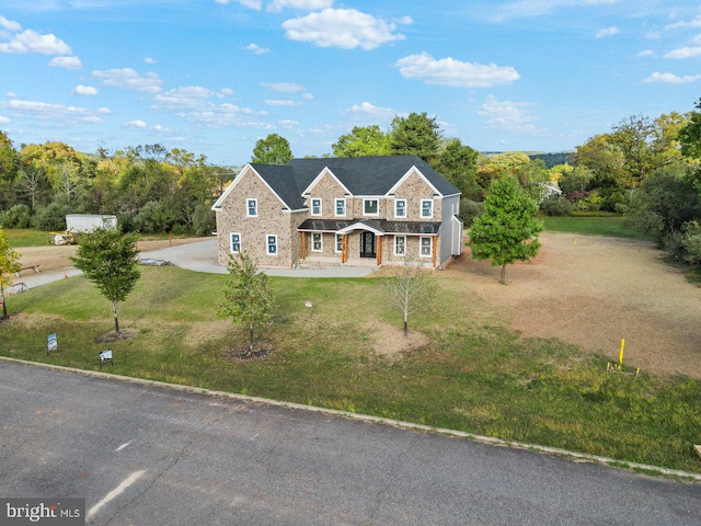 shingle-style home featuring a front yard and stone siding