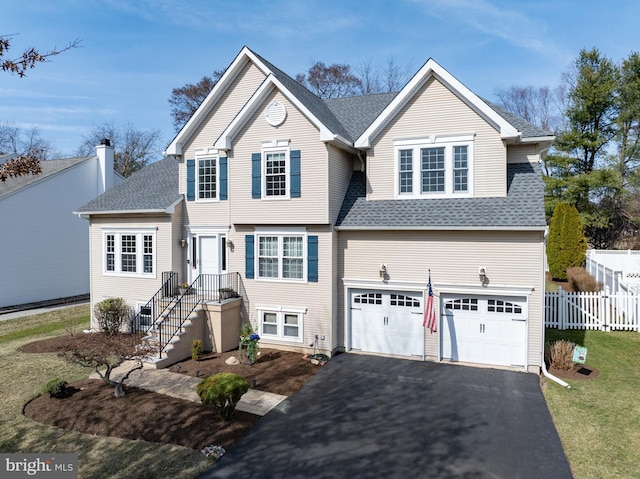 traditional home featuring aphalt driveway, an attached garage, a shingled roof, and fence