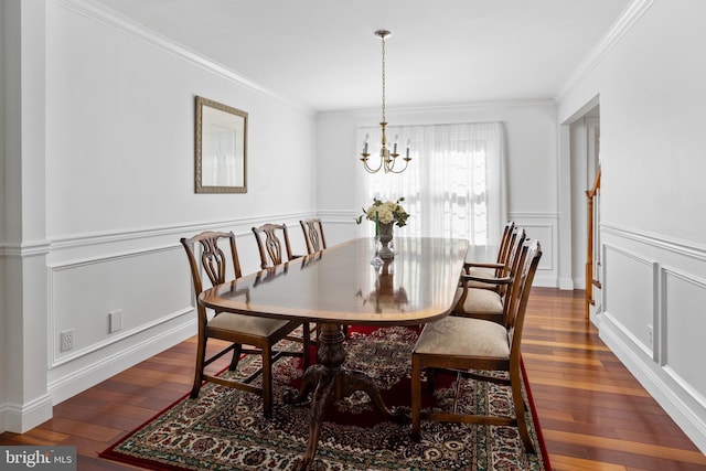 dining space with hardwood / wood-style floors, a wainscoted wall, crown molding, a decorative wall, and a notable chandelier