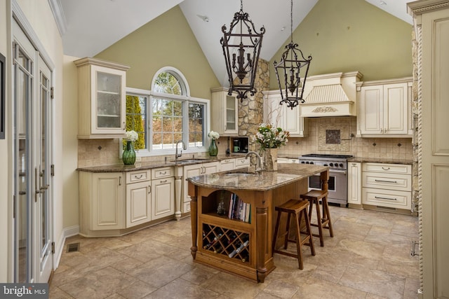 kitchen featuring custom range hood, dark stone countertops, cream cabinets, stainless steel range, and a sink