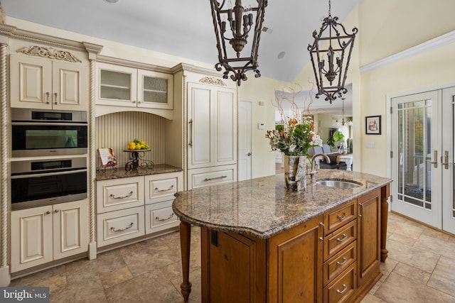 kitchen with brown cabinetry, a sink, cream cabinetry, stainless steel oven, and a notable chandelier