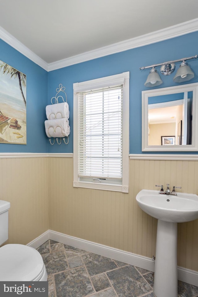 half bath featuring a wainscoted wall, toilet, crown molding, and a sink