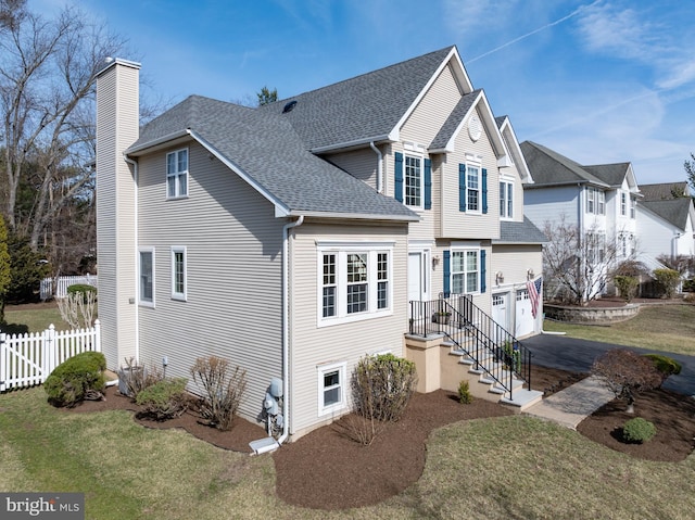 traditional home with fence, aphalt driveway, roof with shingles, a chimney, and an attached garage