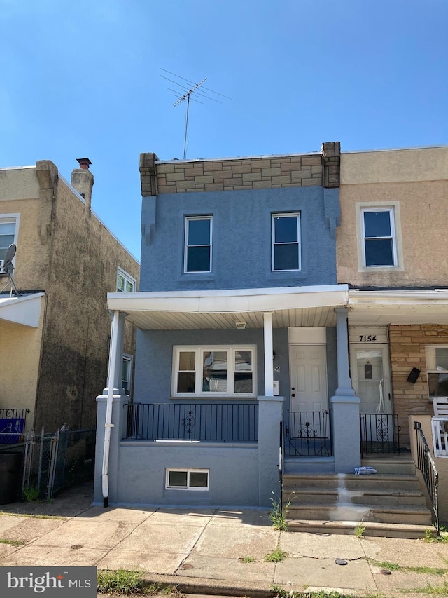 view of property featuring stucco siding, a porch, and fence