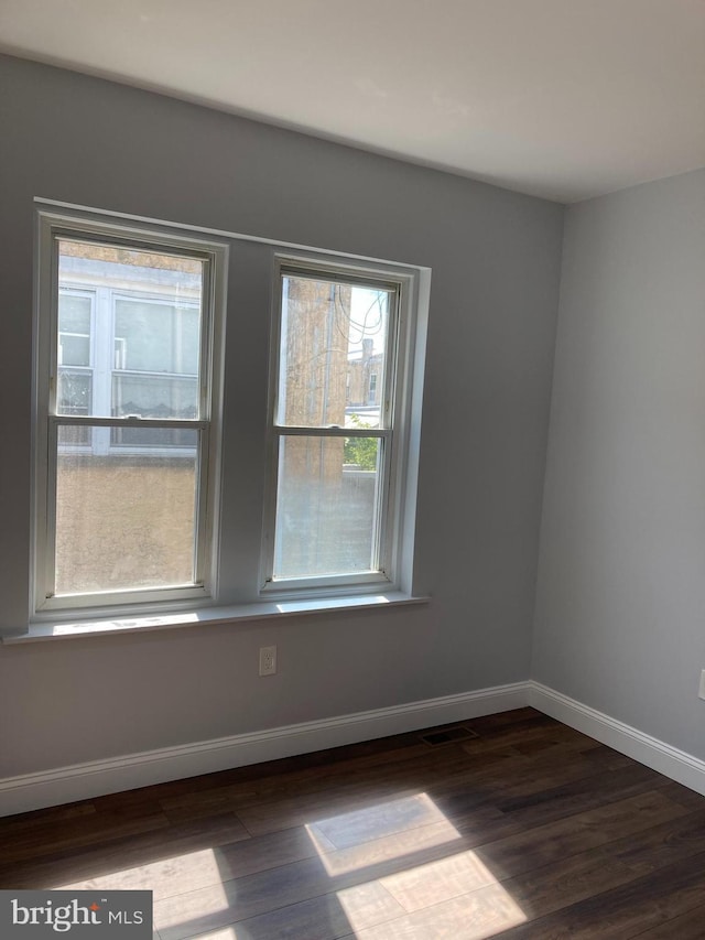 spare room with dark wood finished floors, visible vents, and baseboards