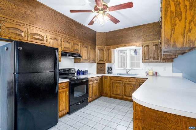 kitchen featuring brown cabinetry, a sink, black appliances, light countertops, and under cabinet range hood