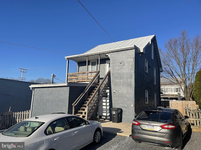 view of front of property featuring stairway, covered porch, concrete block siding, and fence