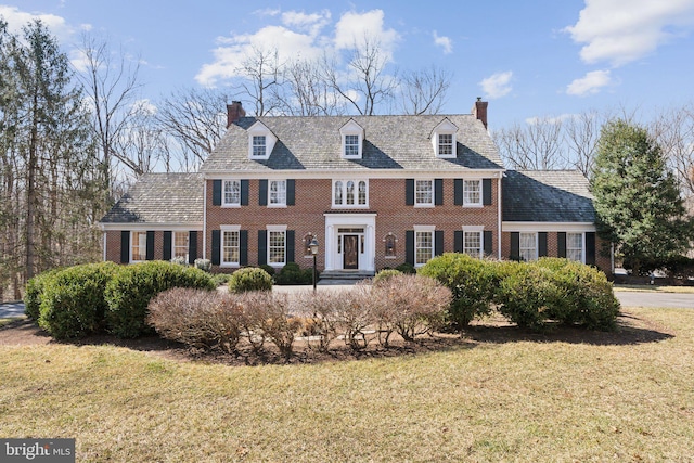 georgian-style home with a front yard, a high end roof, brick siding, and a chimney