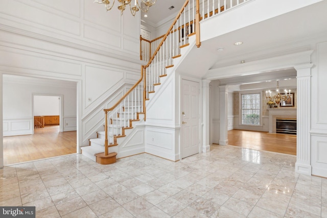 staircase featuring ornamental molding, a high ceiling, an inviting chandelier, a decorative wall, and marble finish floor