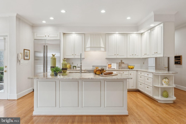 kitchen with light stone countertops, stainless steel built in fridge, custom range hood, light wood-style floors, and crown molding