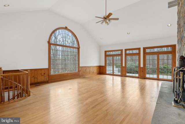 unfurnished living room with wood finished floors, a healthy amount of sunlight, a wainscoted wall, and high vaulted ceiling